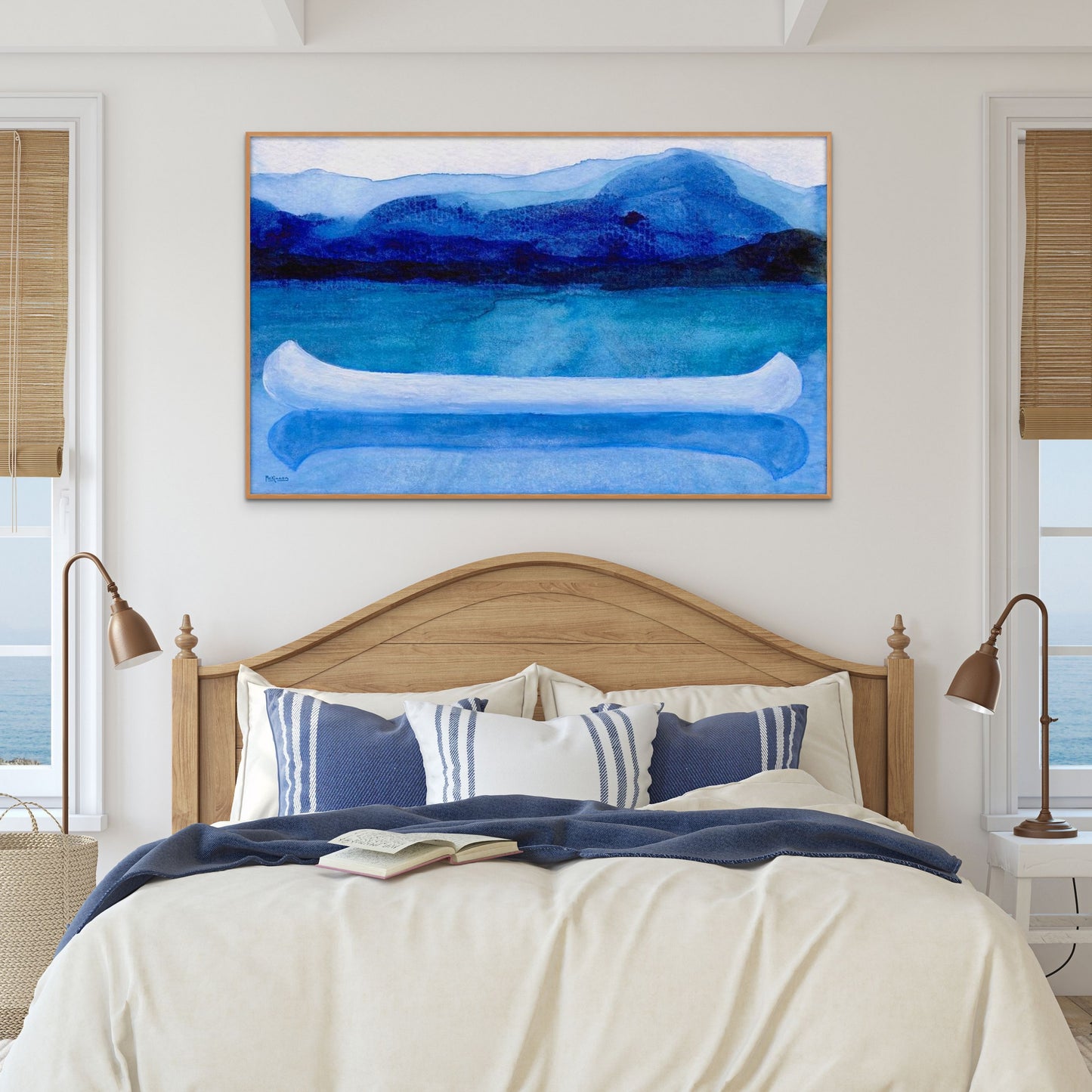 A work of canoeing art by Canadian artist Catherine McKinnon. The watercolor depicts a small white boat, a "canoe", on blue water with a dark blue distant shore and lighter blue distant moutains. The giclee print is framed in natural wood and is mounted on a white wall above a bed in a blue and white coastal themed bedroom.