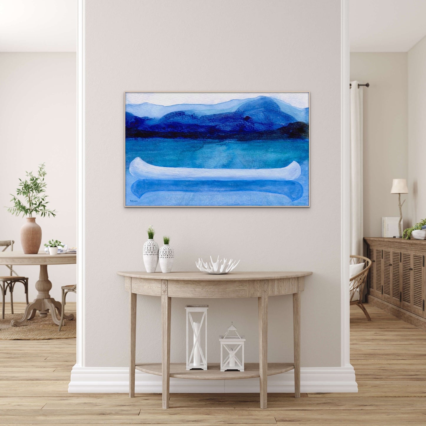A work of canoeing art by Canadian artist Catherine McKinnon. The watercolor depicts a small white boat, a "canoe", on blue water with a dark blue distant shore and lighter blue distant moutains. The giclee print is framed in light-colored wood and is mounted on a light gray wall.